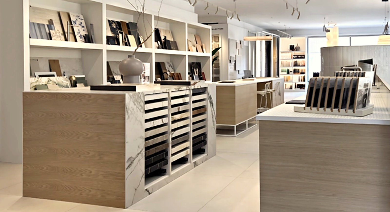 Showroom de carrelage et matériaux : îlots en chêne clair, marbre blanc et présentoirs d’échantillons